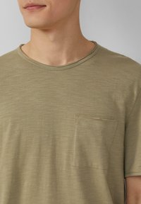 Olijfgroene T-shirt van zachte stof met een ronde hals en een klein borstzakje met een subtiele textuur en stikdetails.