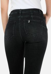 Mustad denim teksad, millel on tihe disain, koos kahe tagatasku, peente õmbluste detailide ja väikesega metalllogo aktsendiga vööl.