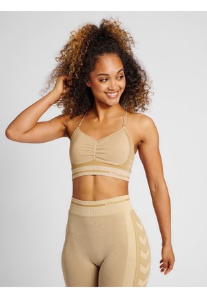 Beige sportcrop top met een geplooide voorkant, dunne bandjes, en bijpassende high-waisted leggings met textuuraccenten en patroon details.