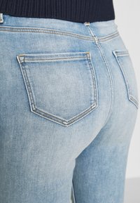 Jeans de mezclilla azul claro con un diseño ajustado, que cuentan con dos bolsillos traseros con detalles de costura en contraste y una ligera textura elástica.