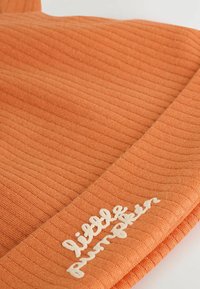 Bonnet orange côtelé avec un revers affichant "petit citrouille" brodé en fil blanc. Tissu doux et texturé.