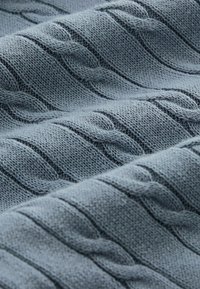 Tessuto in maglia grigia morbida con motivi a treccia in rilievo, superficie texturizzata e un leggero lucido, che mostra delicate pieghe.