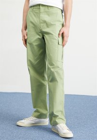 Lys grønne cargo-bukser med en afslappet pasform, der har sidelommer og en subtil tekstur. Parret med hvide lavtoppede sneakers.