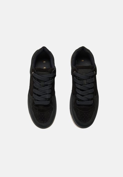 Paire de baskets noires avec des lacets foncés vues de dessus sur un fond gris clair, indiquant la taille 43 à l’intérieur de chaque chaussure.