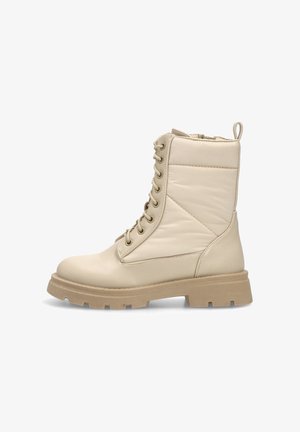 Botas de tobillo beige con un acabado de cuero suave, que presentan un cierre con cordones en la parte frontal, un collar acolchado y una suela de goma gruesa y texturizada.