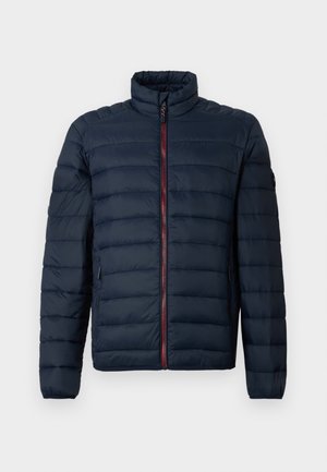 Navy pufferjacka med horisontell quiltad mönster, hög krage, framdragkedja och röda detaljer. Har sidofickor och elastiska muddar.
