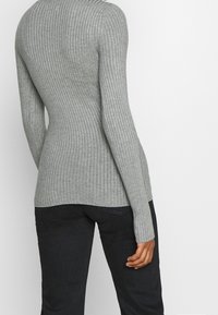 Top lungo a maniche ribbed grigio con design aderente, scollo rotondo e maniche allungate, abbinato a jeans scuri.