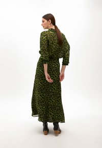 Pitkä vihreä mekko, jossa on leopardikuosiset yksityiskohdat, valmistettu läpivalaisevasta kankaasta. Mekossa on kapeaksi nyöritetty vyötärö, kolmen neljänneksen hihat ja virtaava hame.
