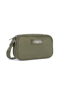 Borsetta in nylon verde con chiusura a zip, forma rettangolare, e etichetta in pelle con la scritta "LANCASTER PARIS." Include un cinturino da polso staccabile.
