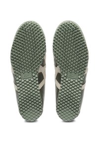 Green sneaker soles with a textured rubber pattern. Features beige accents and includes branding. Designed for optimal traction.