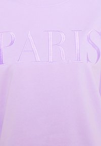 Sudadera lila con el texto "PARIS" bordado. Textura suave con cuello redondo y un corte ligeramente holgado. Sin patrones ni acentos adicionales.