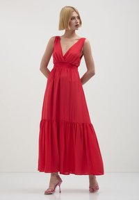 Abito maxi rosso con scollo a V profondo, vita arricciata e gonna a strati. Caratterizzato da un tessuto morbido e leggero e da una silhouette fluida.