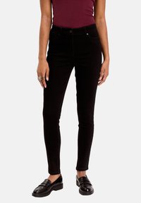 Jean skinny en denim noir, taille haute avec poches avant et arrière, associés à des mocassins noirs. Texture lisse avec un minimum de détails.