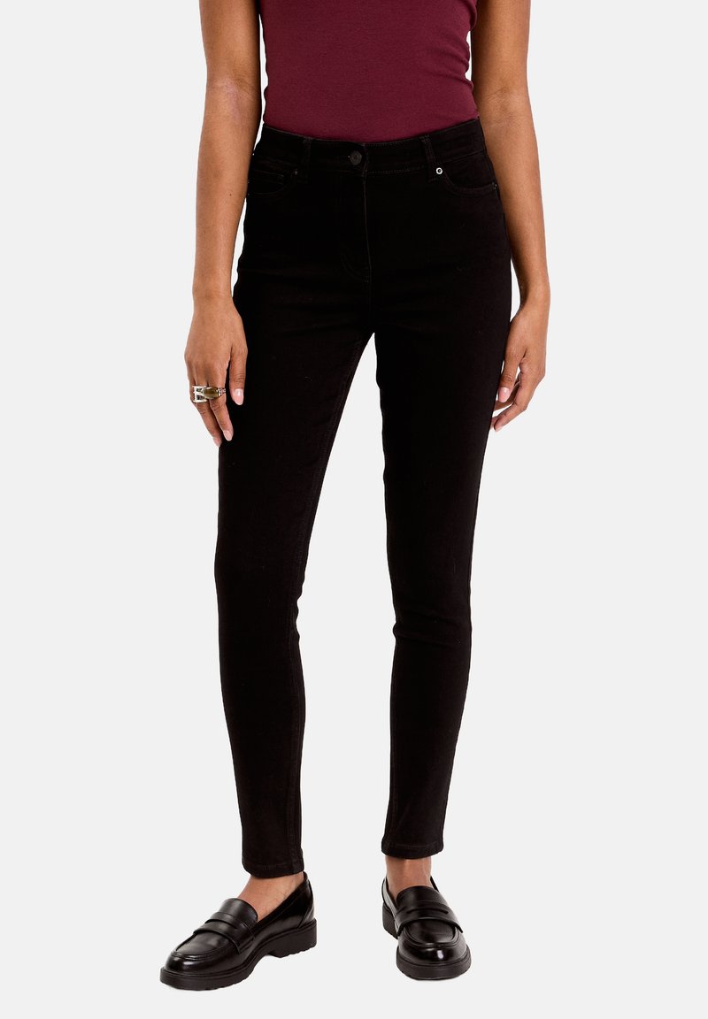 Jean skinny en denim noir, taille haute avec poches avant et arrière, associés à des mocassins noirs. Texture lisse avec un minimum de détails.