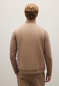 Beige Sweatshirt mit hohem Kragen, glattem Stoff, gerippten Bündchen und Saum. Die Rückseite weist ein nahtloses Design und einen minimalistischen Stil auf.