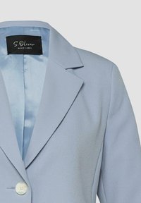 Veste blazer bleu clair avec col à revers cranté et fermeture par un bouton blanc unique, montrant partiellement le devant et l'épaule.