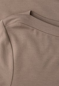 Beiger Stoff mit glatter Textur, mit geschichteten Abschnitten und einem geschwungenen Ausschnitt. Nahtdetails sind entlang der Kanten sichtbar.