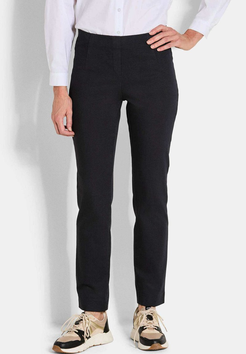 Zwarte strakke broek met een gladde textuur, hoge tailleband en zijzakken, gecombineerd met beige en zwarte sneakers.