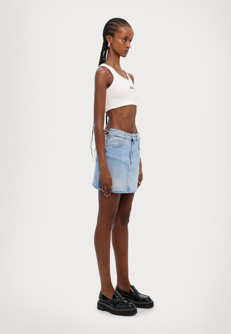 Džínsová minisukňa vo svetlomodrej farbe, s priliehavým strihom a predným zapínaním na gombík. Kombinovaná s bielym krátkym tielkom a čiernymi platformovými topánkami.