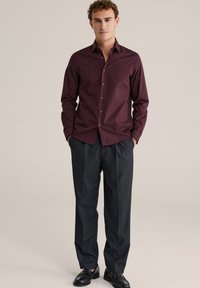 Burgundiškas mygtukų marškinys, pagamintas iš lygios medvilnės, derinamas su tamsiai pilkais pritaikytais kelnėmis. Juodi loaferiai užbaigia aprangą.