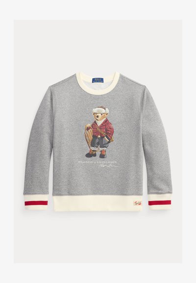 Grå genser med en bjørneillustrasjon i rutete skjorte, snøsportutstyr og kjelke. Kremfarget krage og mansjetter med røde detaljer.