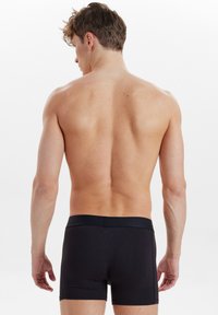 Schwarze Boxershorts mit glatter Textur und einem kontrastierenden Bund. Das Design ist figurbetont mit kurzer Beinlänge und ohne sichtbare Muster.