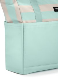 Ljusblå och beige randig bastväska med en synlig sidoficka och vävd handtagsrem, med en svart varumärkesetikett.