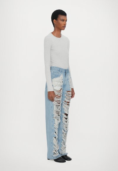 Camisola de manga longa cinza claro emparelhada com jeans desgastados azuis claros, apresentando grandes rasgos e bordas desfiadas. Modelo usando calçado preto.