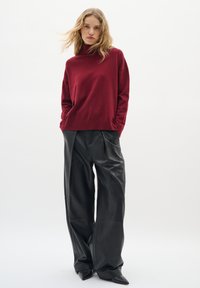 Pull col montant bordeaux associé à un pantalon large en cuir noir ; textures lisses et coupe ajustée avec des chaussures noires pointues.