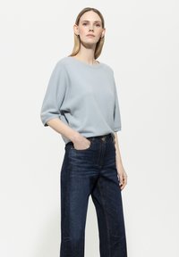 Hellblauer, kurzärmeliger Pullover aus weichem Material; kombiniert mit hochgeschnittenen, dunkelblauen Jeans aus Denim mit frontalen Taschen und Stickdetails.