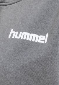 Grå sweatshirt med en texturerad tyg och en vit "hummel" logotyp tryckt framträdande på framsidan.