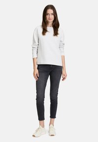 Un haut à rayures blanches et grises à manches longues associé à un jean slim foncé et des baskets claires, le tout sur fond uni.
