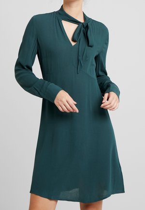 Vestido teal hasta la rodilla con detalle de cuello atado, mangas largas y escote en V. Tela suave y lisa con una silueta fluida.