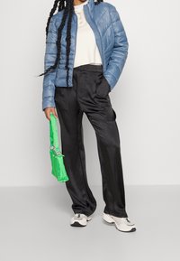 Ljudblå puffjacka, vit skjorta med krage, svarta satinbyxor, grön handväska och grå sneakers. Texturerade material, avslappnad passform.