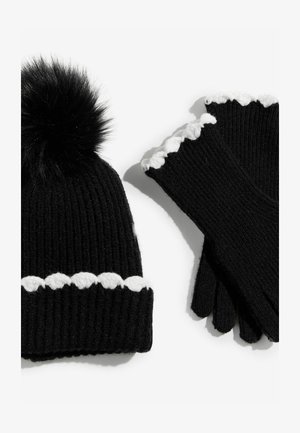 Fekete, kötött sapka szőr pom-pommal és fehér, hullámos szegéllyel, fekete kesztyűvel párosítva, szintén hullámos fehér díszítéssel.