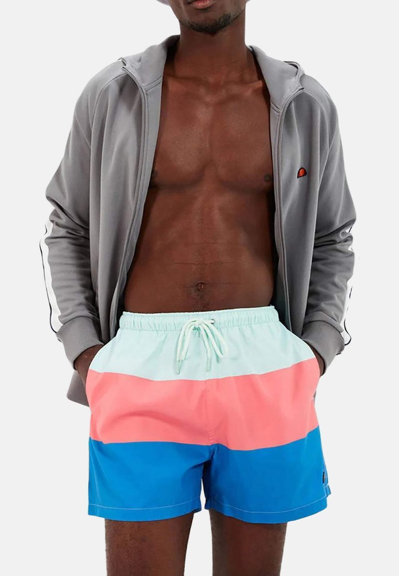 Chaqueta de zip en gris claro con acentos negros, combinada con pantalones cortos de baño multicolores que presentan rayas horizontales en azul claro, rosa y azul.