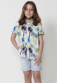 Camisa de manga corta de tejido ligero con un estampado de palmeras multicolores sobre un fondo crema, combinada con pantalones cortos azul claro.