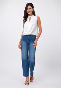 White sleeveless top with a keyhole neckline, paired with high-waisted blue jeans. The outfit is complemented by black strappy sandals.