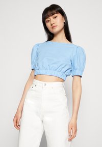 Top curto azul claro com mangas bufantes e cintura elástica, combinado com jeans brancos de cintura alta. Textura suave, design simples.