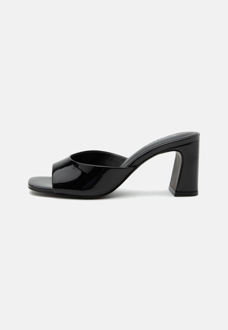 Mule noire en cuir verni à bout ouvert avec une large bride et un talon bloc mi-haut massif sur fond blanc.