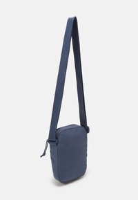 Mörkblå crossbody-väska i texturerat tyg, med rektangulär form, justerbar rem och dragsko-stängning på ena sidan.