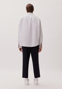 Camicia a righe bianca e blu navy con una vestibilità ampia, dotata di maniche lunghe e spacchi laterali. Abbinata a pantaloni scuri e sneakers bianche.