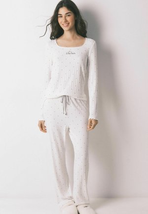 Hvide pyjamas med tynde, lodrette striber og små sorte prikker. Lange ærmer, bred halsudskæring, bindebånd i taljen og flæsekant på ærmeenderne.