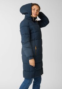 Marine blauwe pufferjas met een capuchon, voorzien van een gewatteerde textuur, voorzakken met rits en elastische manchetten. De capuchon heeft een trekkoord voor aanpassing.