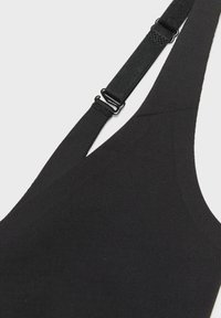 Gros plan d'une coque de soutien-gorge en tissu noir avec une bretelle réglable et un curseur métallique sur un fond clair.