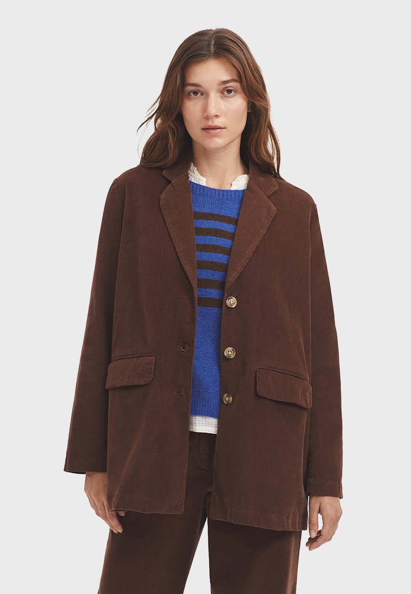 Blazer de pana marrón con solapas con muesca, dos bolsillos delanteros y tres botones. Superpuesto a un suéter a rayas azules que presenta un tejido texturizado.