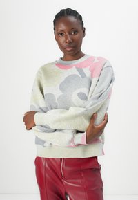 Felpa grigia chiaro con motivi floreali rosa e grigi, caratterizzata da un collo rotondo e polsini a costine. Abbinata a pantaloni in pelle bordeaux.