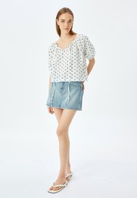 Witte blouse met marineblauw geometrisch patroon, korte pofmouwen en trekkoorden. Gepaard met een lichtblauwe denim minirok en witte sandalen.