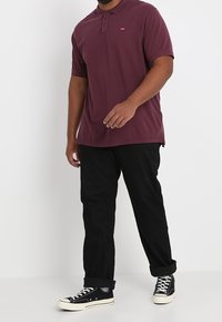 T-shirt polo bordeaux avec patte de boutonnage à deux boutons, manches courtes et un petit logo. Assorti avec un pantalon noir et des baskets montantes noires.