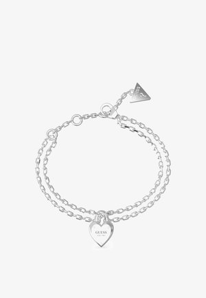 Silberne Kettenarmband mit zwei Schichten, einem herzförmigen Anhänger mit der Gravur 'GUESS EST. 1981' und einem triangularen Anhänger als Akzent.